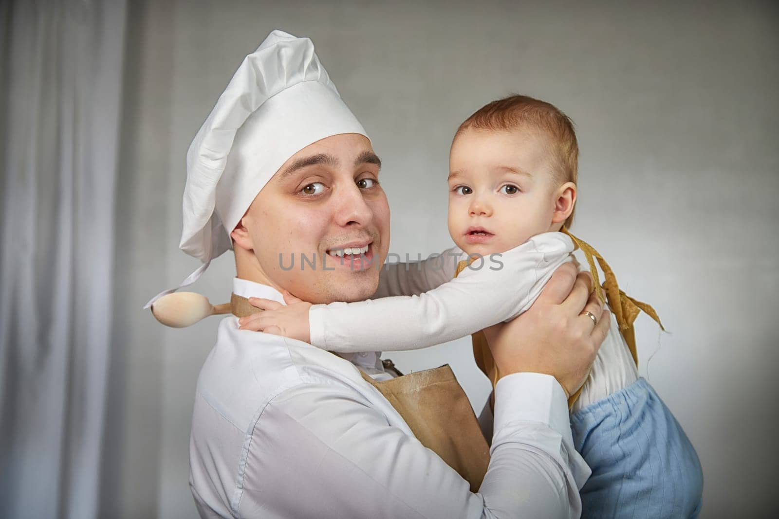 A family enjoys a fun cooking session, playfully covered in flour while engaging with their little ones in a warm kitchen. Father and son having fun