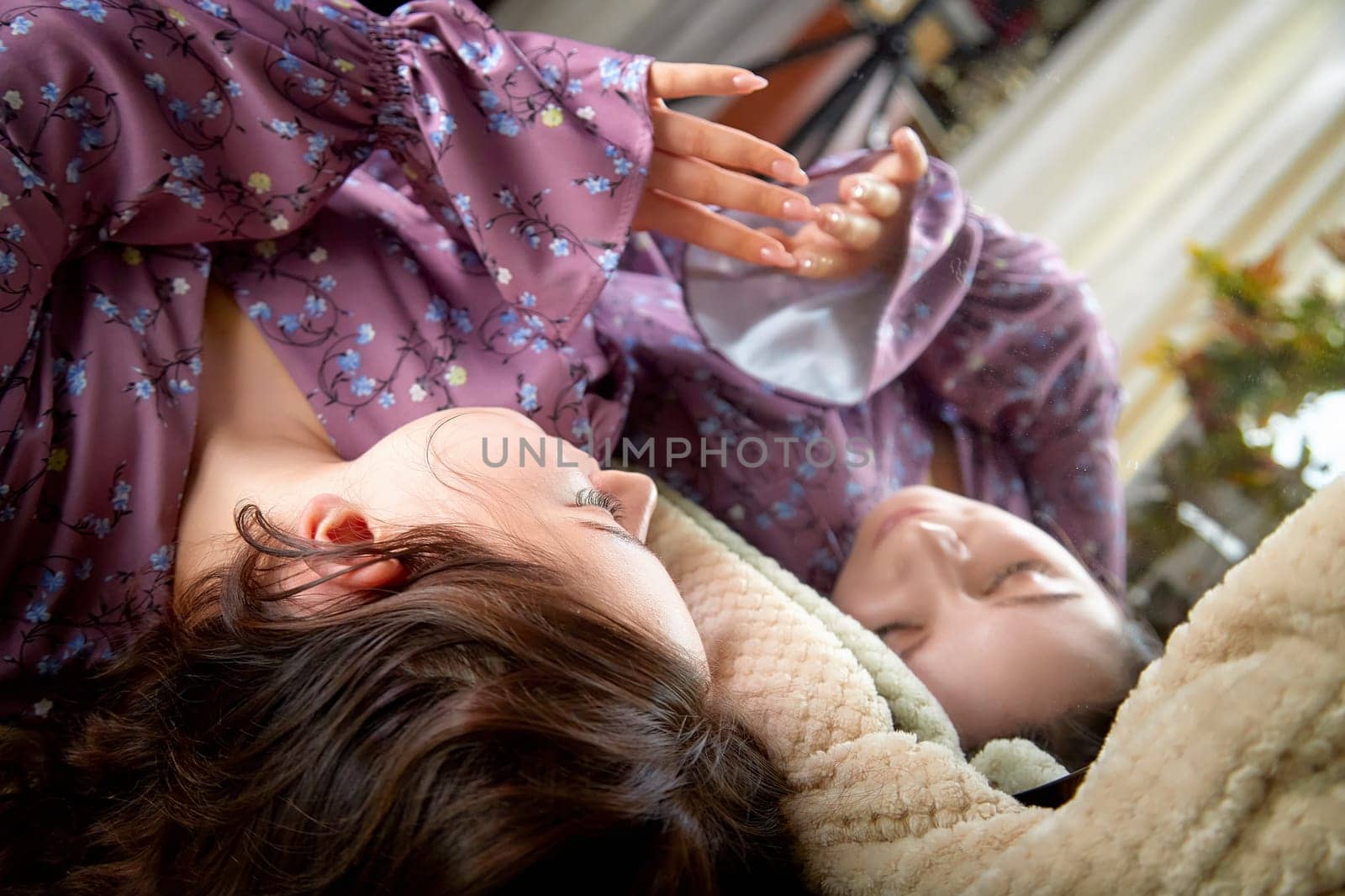 Two people comfortably recline on a couch, engaging in a tender moment while surrounded by soft blankets in a warm, inviting space.