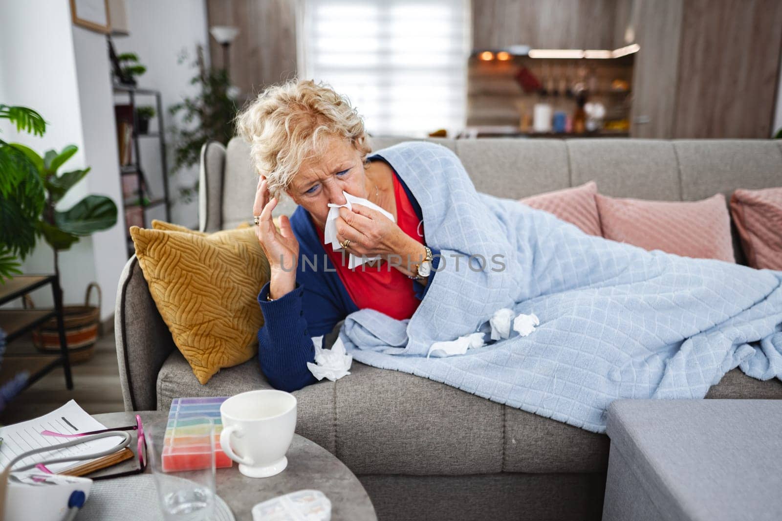 Older woman relaxes on sofa, feeling unwell and surrounded by tissues.