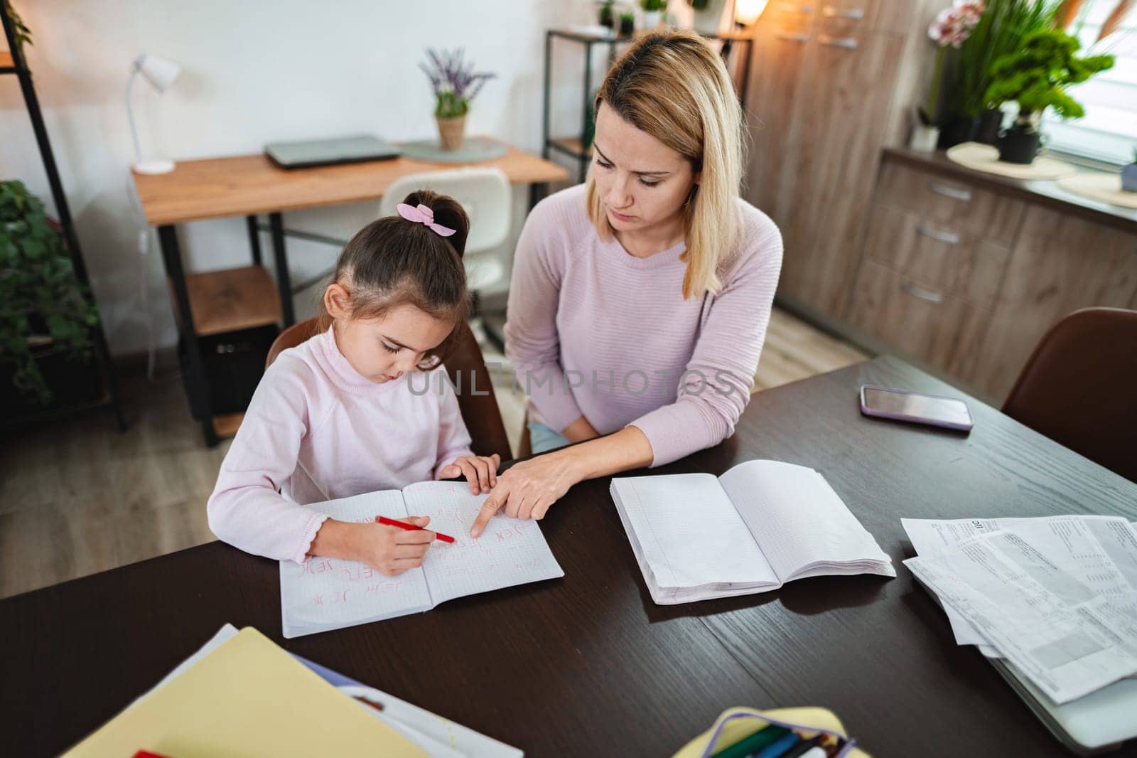 A young girl learns as her mother assists with homework at a table.