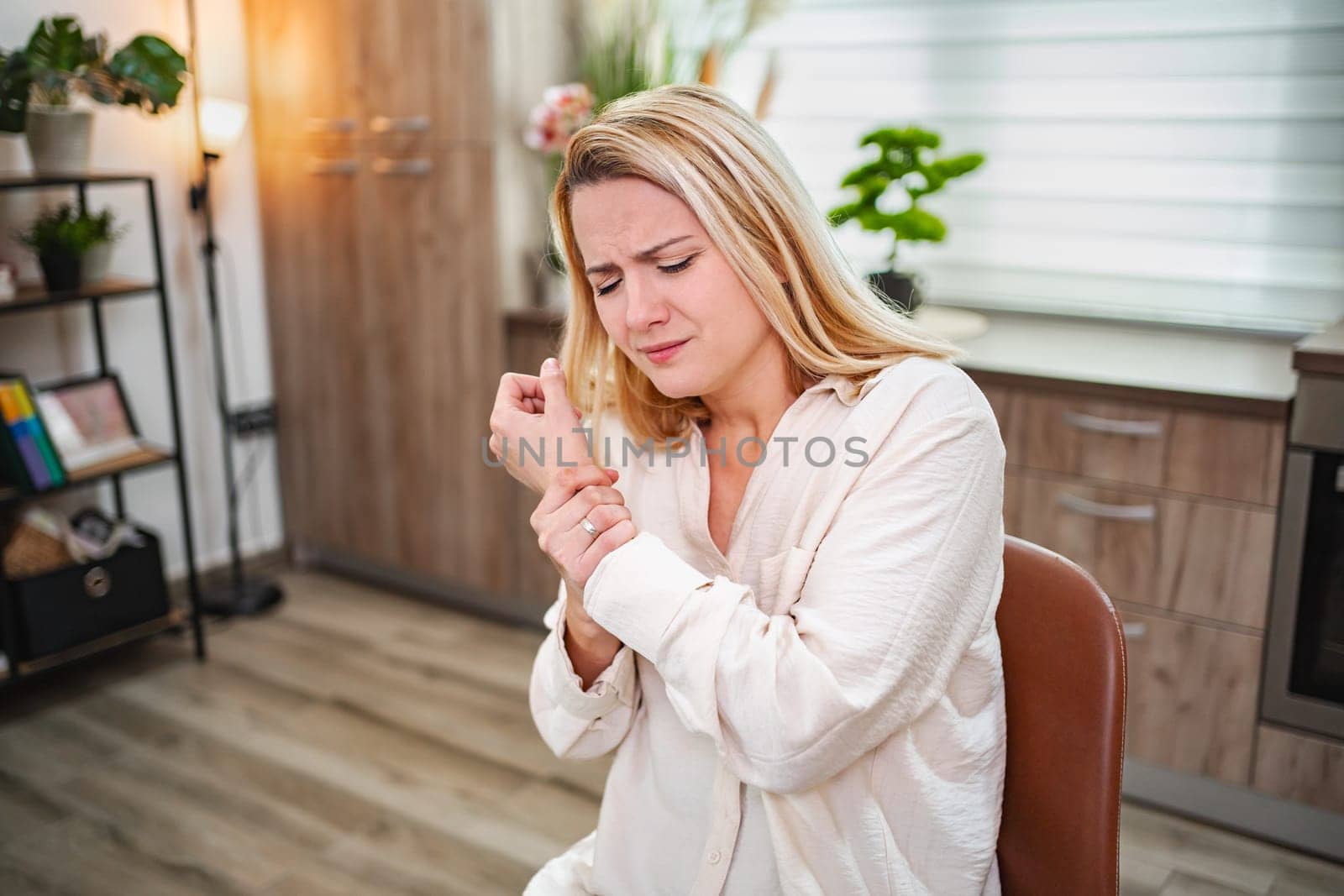 Young woman seated, wincing in discomfort while holding her wrist.