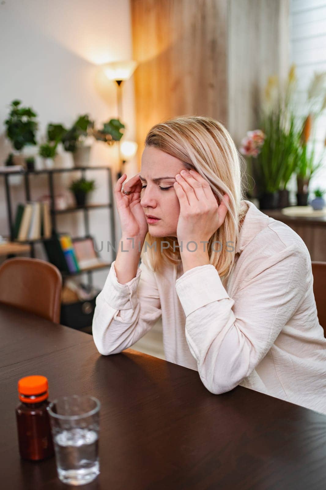 Young woman rests her head in her hands, showing signs of discomfort in a home.