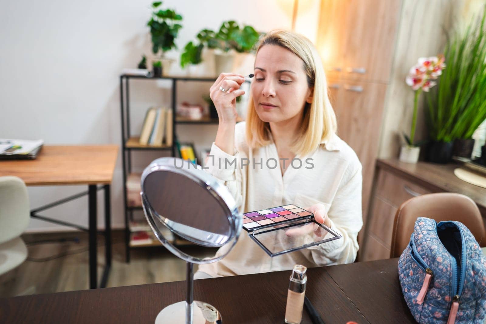 A woman focuses on her makeup application with a colorful palette.