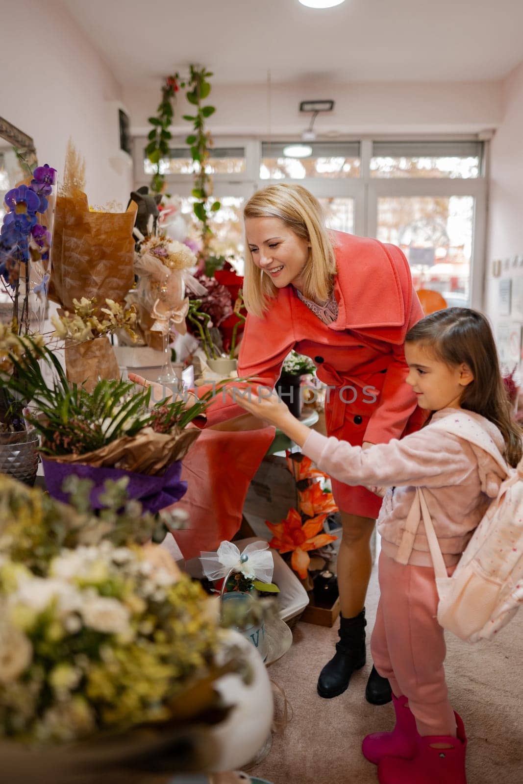 In a vibrant floral shop, a mother and her daughter share a delightful experience as they admire and choose colorful flowers together. Their laughter fills the air on a lovely afternoon.