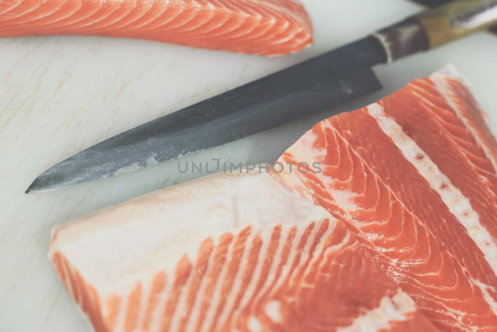 Asian chef slice salmon by knife on boad for japanese food delicacy consisting sashimi salmon of very fresh raw salmon fish sliced into thin pieces serving with radish sliced in japanese restaurant