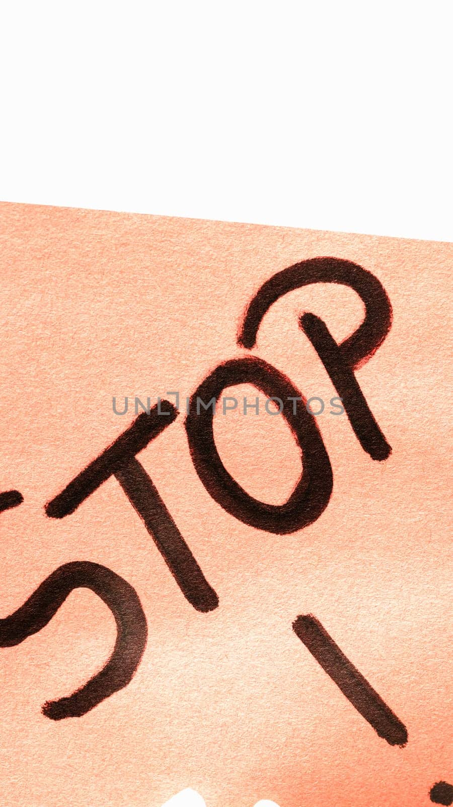 Stop handwriting text close up isolated on orange paper with copy space. Writing text on memo post reminder by vladispas