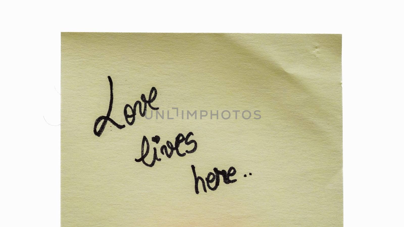 Love lives here handwriting text close up isolated on yellow paper with copy space. by vladispas