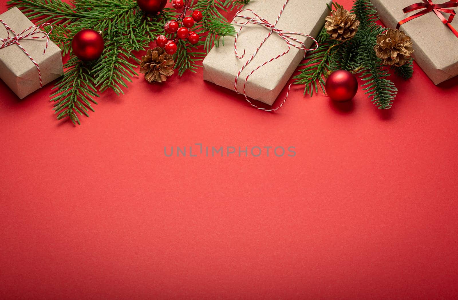 Christmas or New Year celebration red paper festive background with decoration fir tree, wrapped present boxes, cones, berries, sparkly red balls. Space for text. by its_al_dente