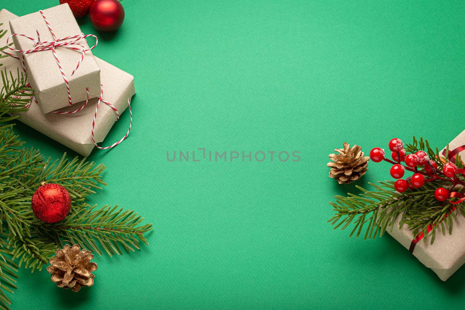 Christmas or New Year celebration green paper festive background with decoration fir tree, present boxes, cones, berries, sparkly red balls. Space for text..