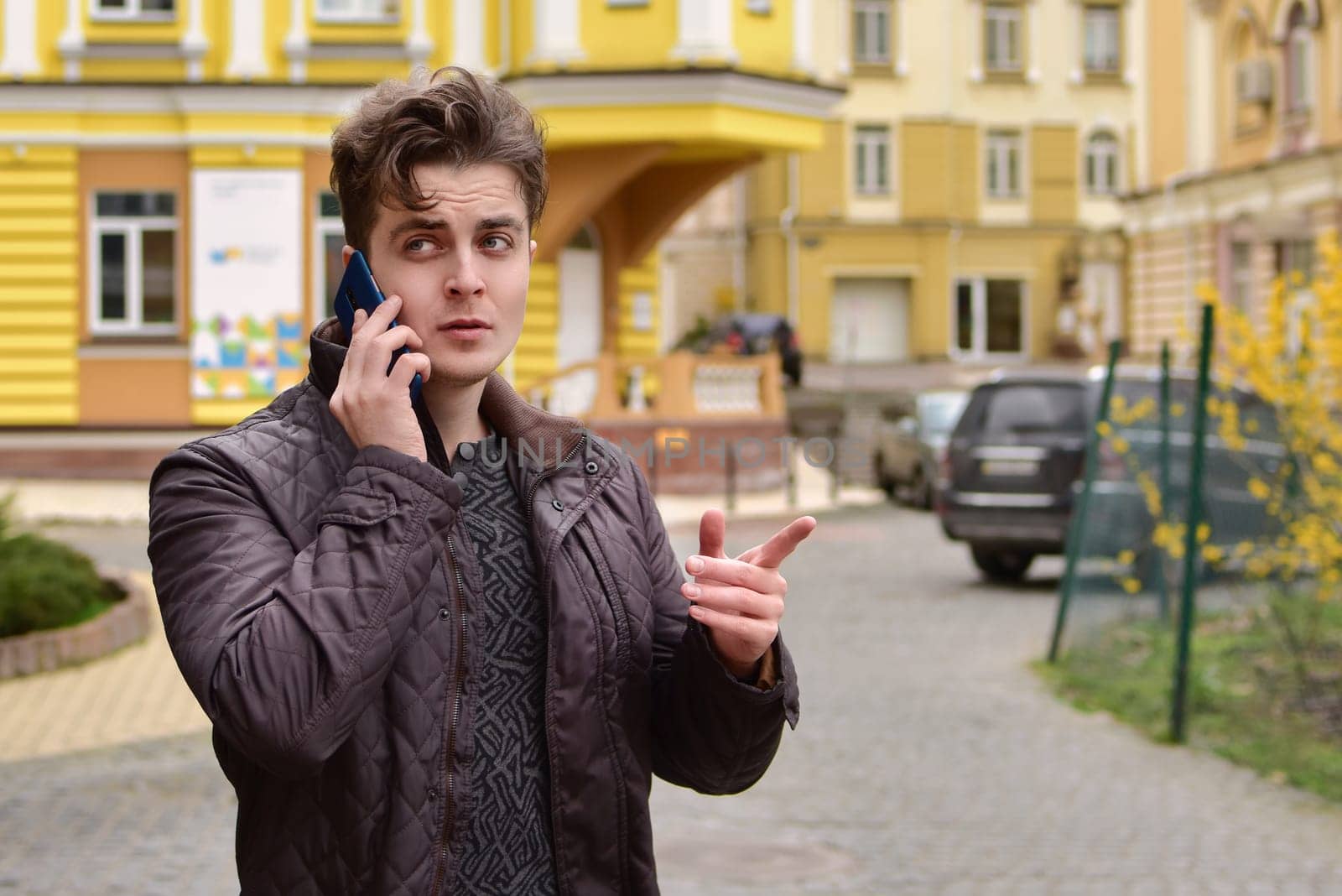 An attractive man with curly hair in an autumn jacket talking on the phone discussing important business