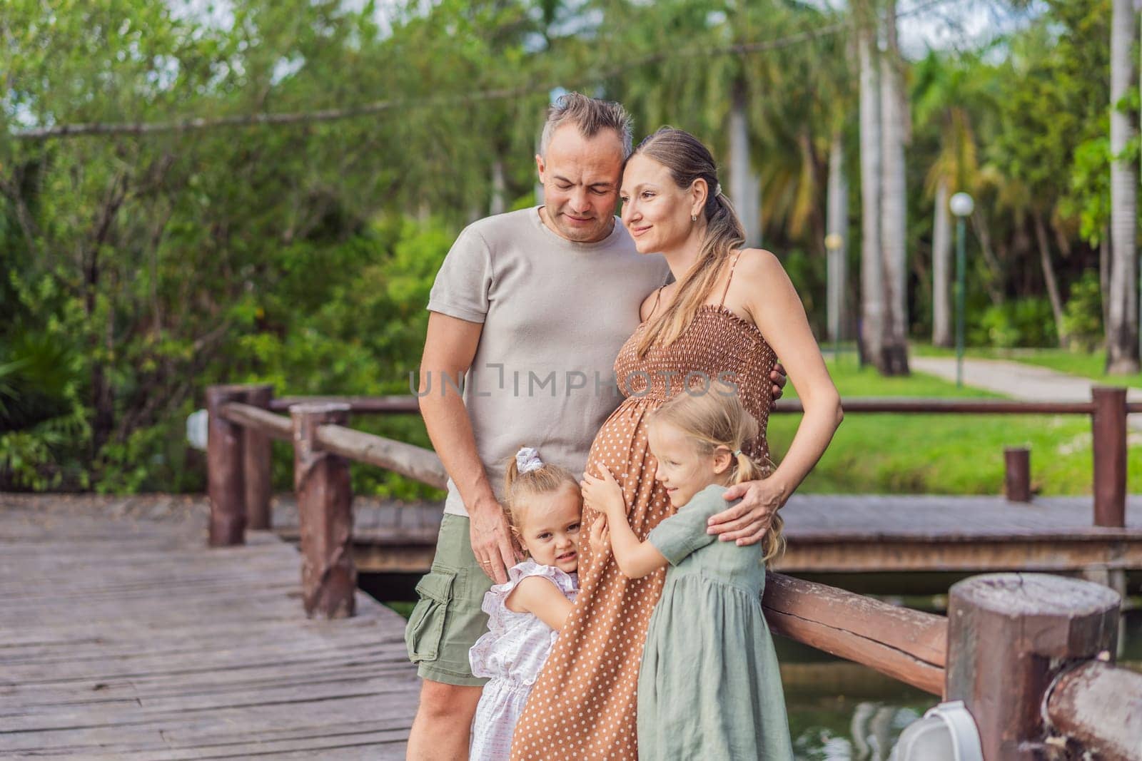 A happy, mature couple over 40 with their two daughters, enjoying a leisurely walk in a park, their joy evident as they embrace the journey of pregnancy later in life.
