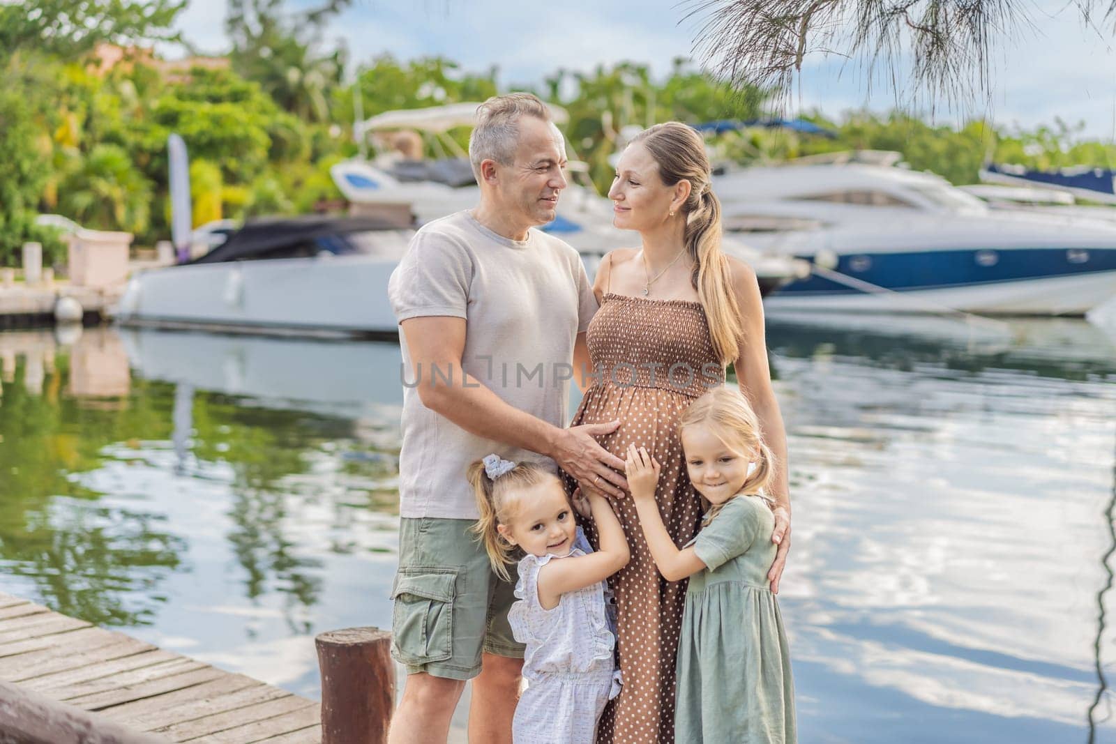 A happy, mature couple over 40 with their two daughters enjoying a leisurely walk on the waterfront, their joy evident as they embrace the journey of pregnancy later in life.