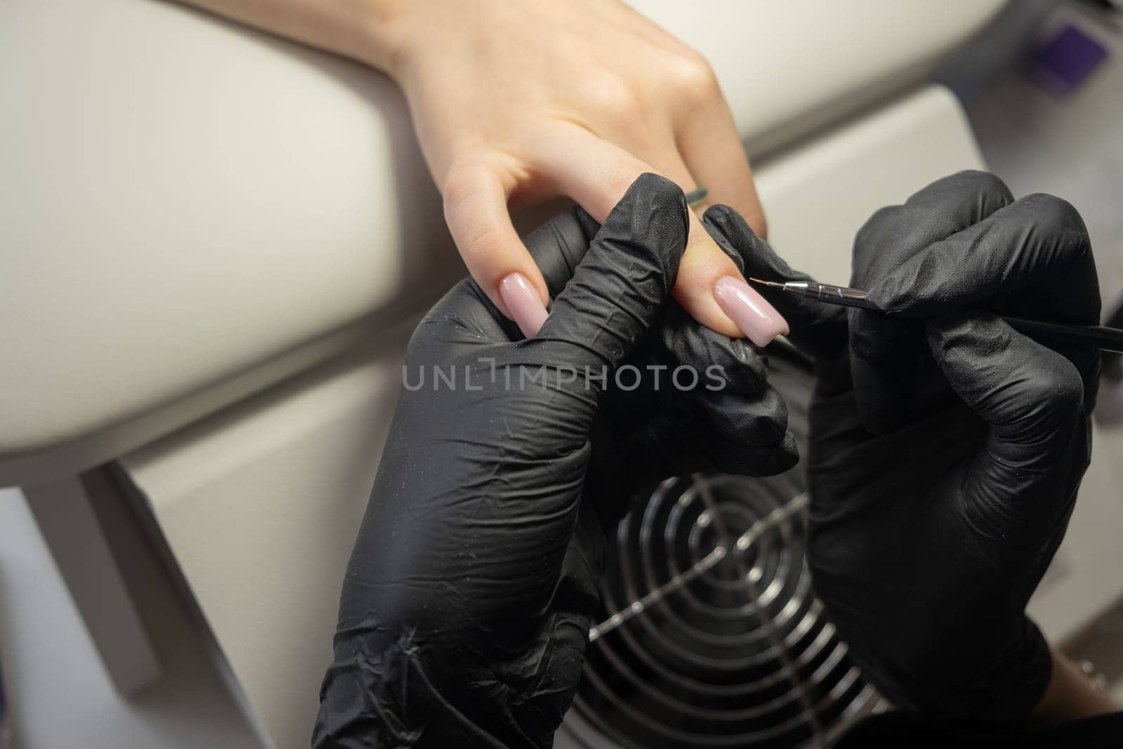 Female hands and tools for manicure, process of performing manicure in beauty salon. Nail care procedure in a beauty salon. Gloved hands of an experienced manicurist in gloves are varnished nails