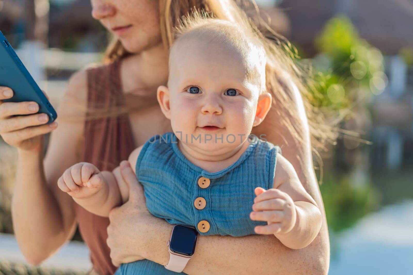 Mom holds her adorable baby while holding a smartphone.