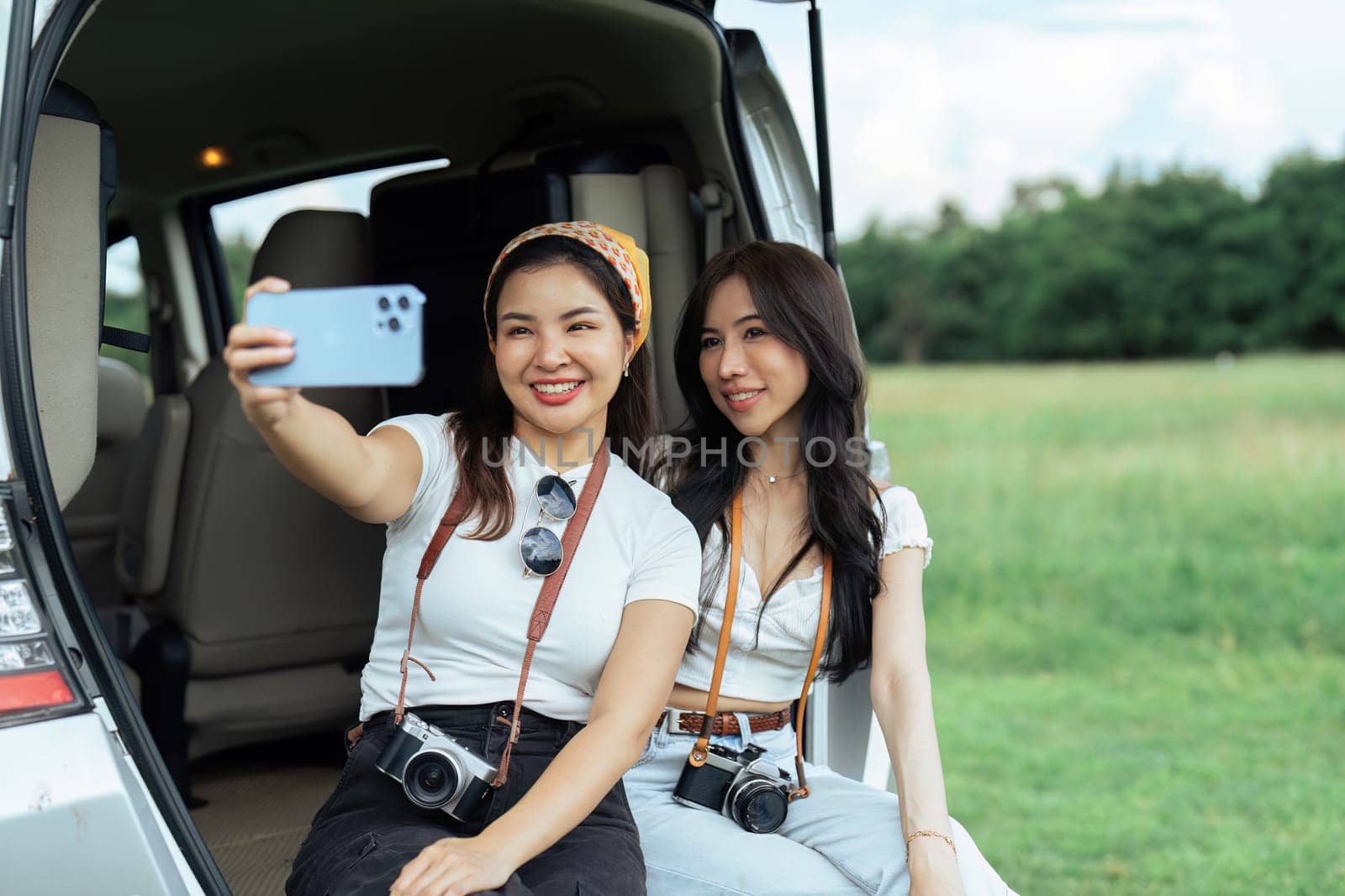 Two women friends and open trunk of car to sit back and relax after reaching rest place.