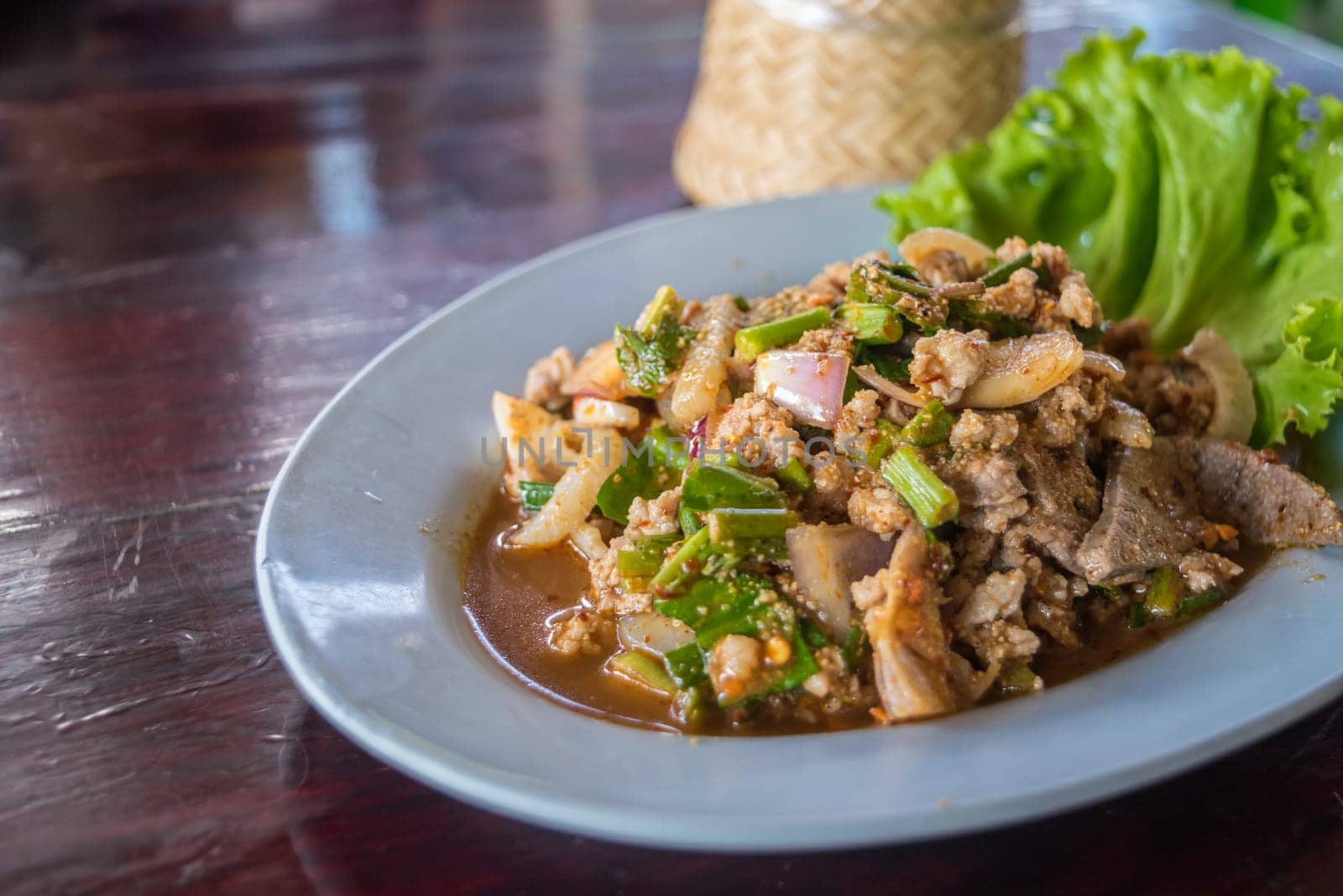 Spicy minced pork salad or Ground pork salad (Laab) is a Thai food for health consists of pork, ground rice, chili, lemon, onion and herb mixed in plate on a wood table at Thai street food