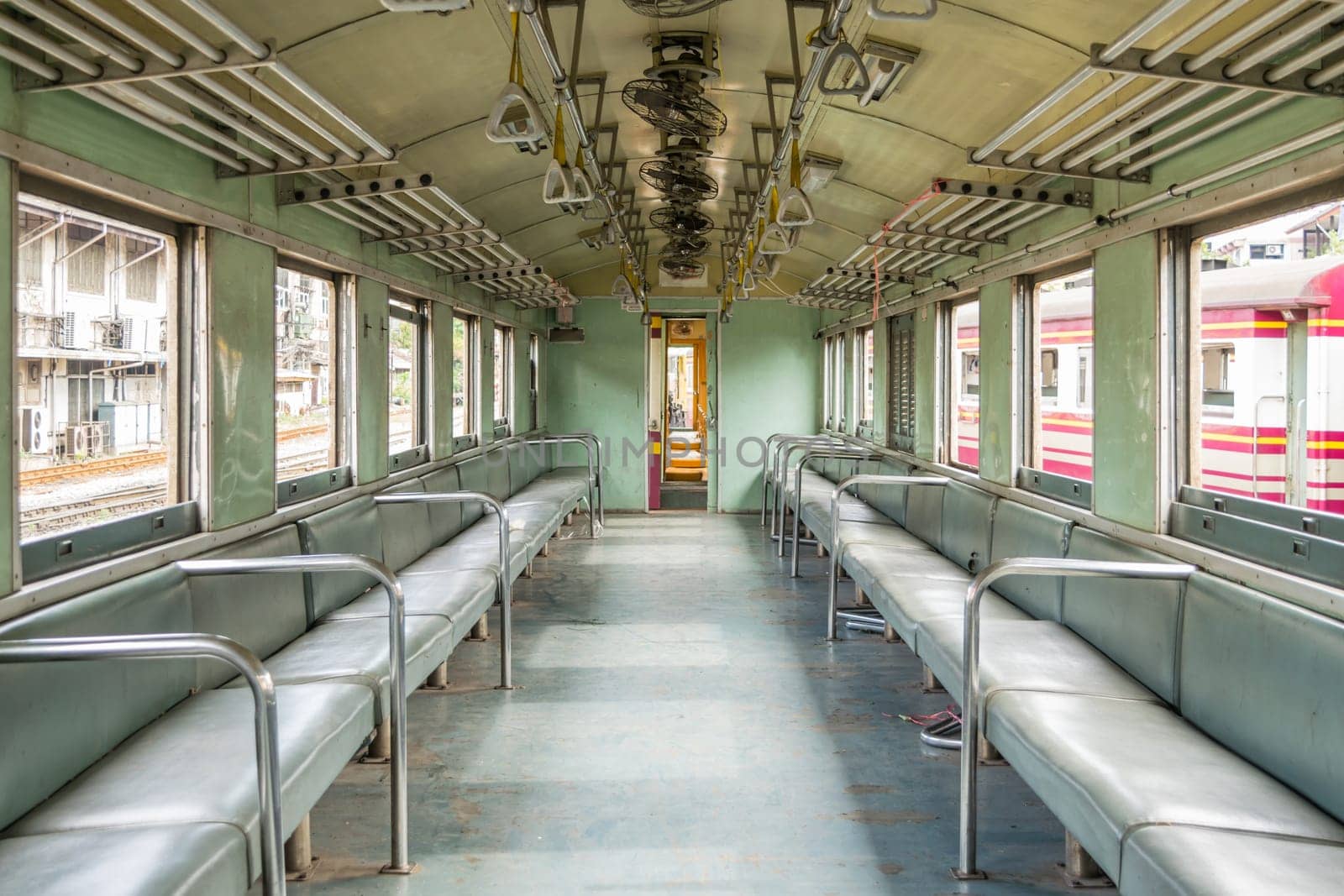 Inside of old public Thai railway train cabin with seats, handrails, fan and interior in vintage style service for passenger transport