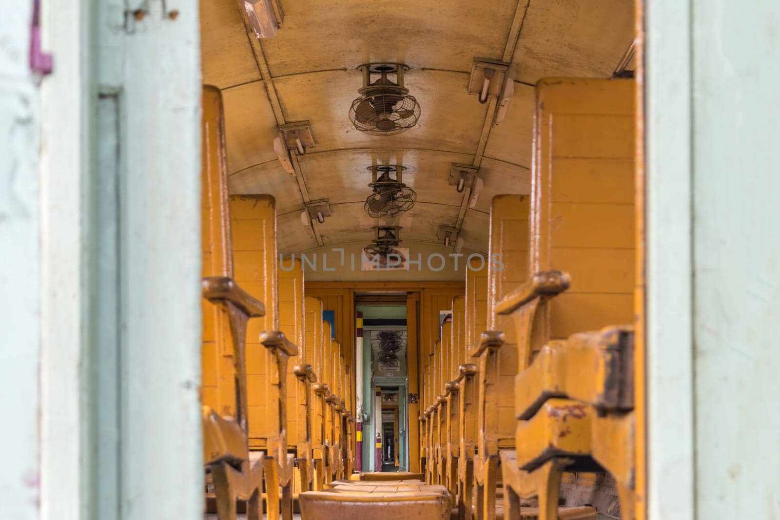 Inside of old public Thai railway train cabin with seats, handrails, fan and interior in vintage style service for passenger transport