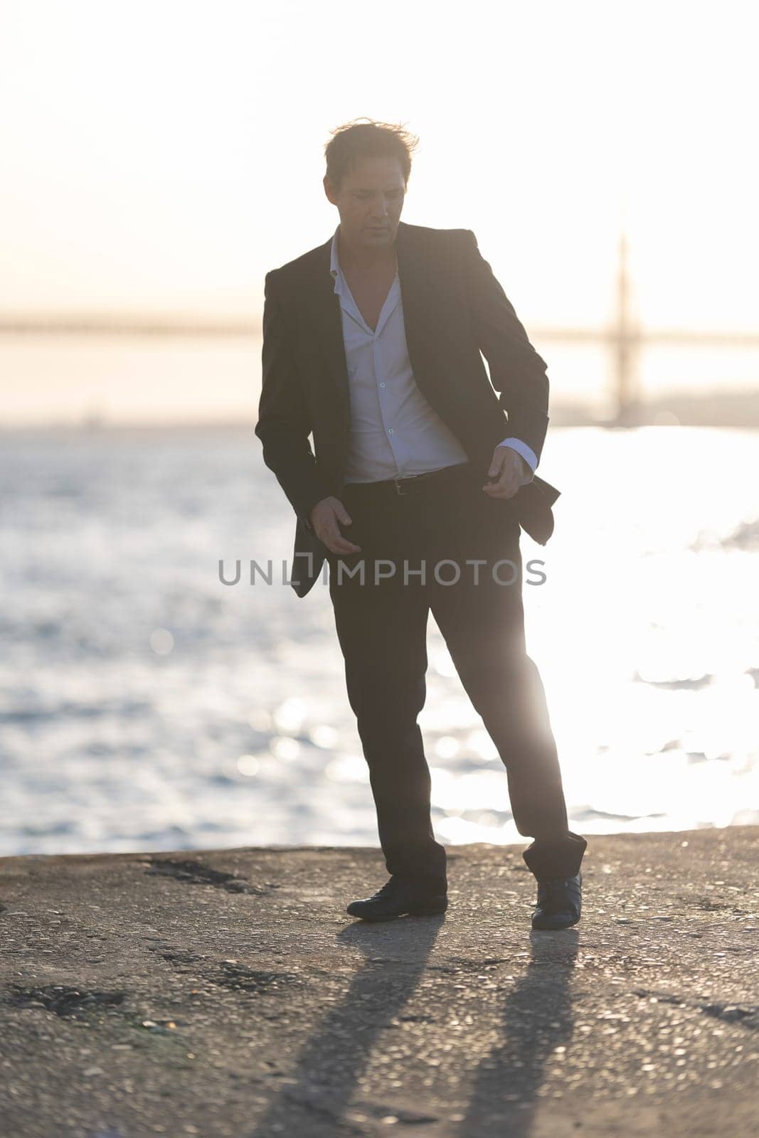 Businessman is striking a pose by the water at sunset