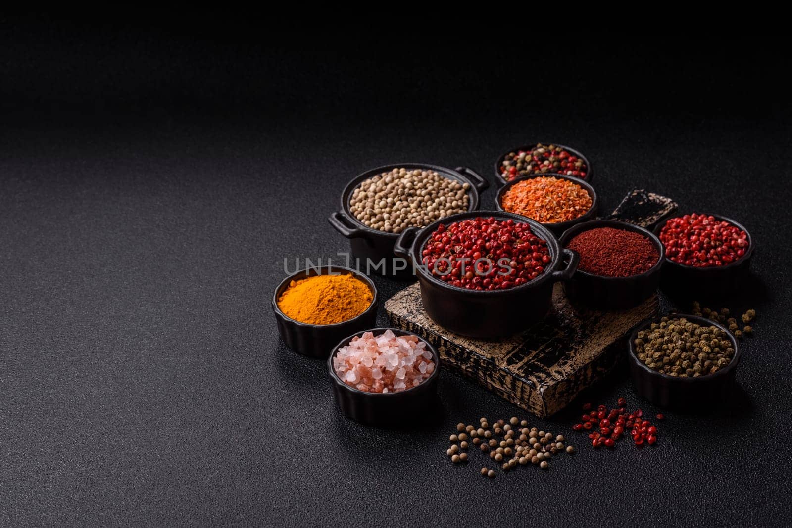 Variations of spices, allspice, turmeric, paprika, salt in ceramic bowls on a dark concrete background