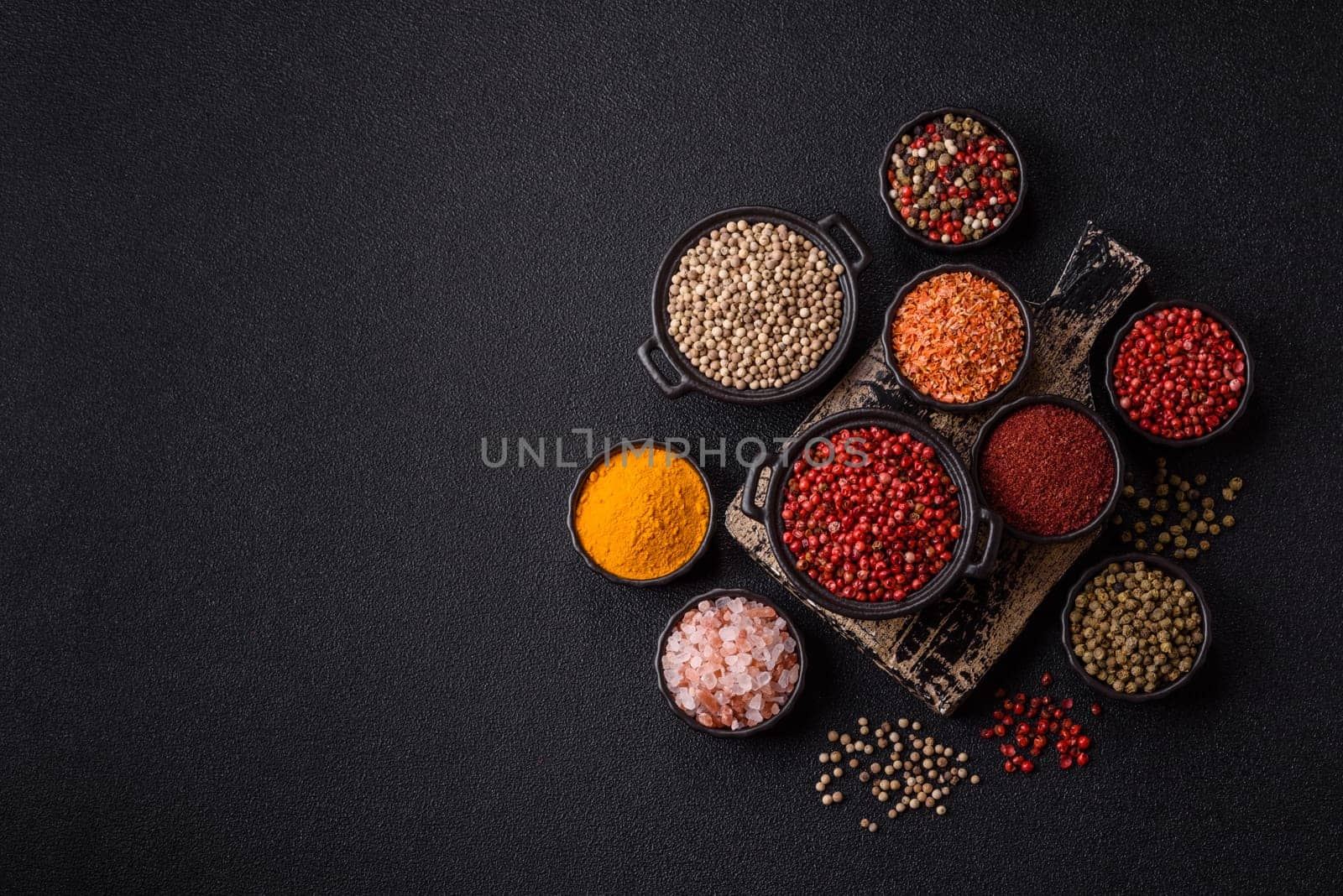Variations of spices, allspice, turmeric, paprika, salt in ceramic bowls on a dark concrete background