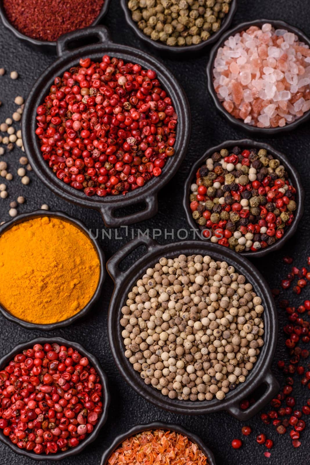 Variations of spices, allspice, turmeric, paprika, salt in ceramic bowls on a dark concrete background
