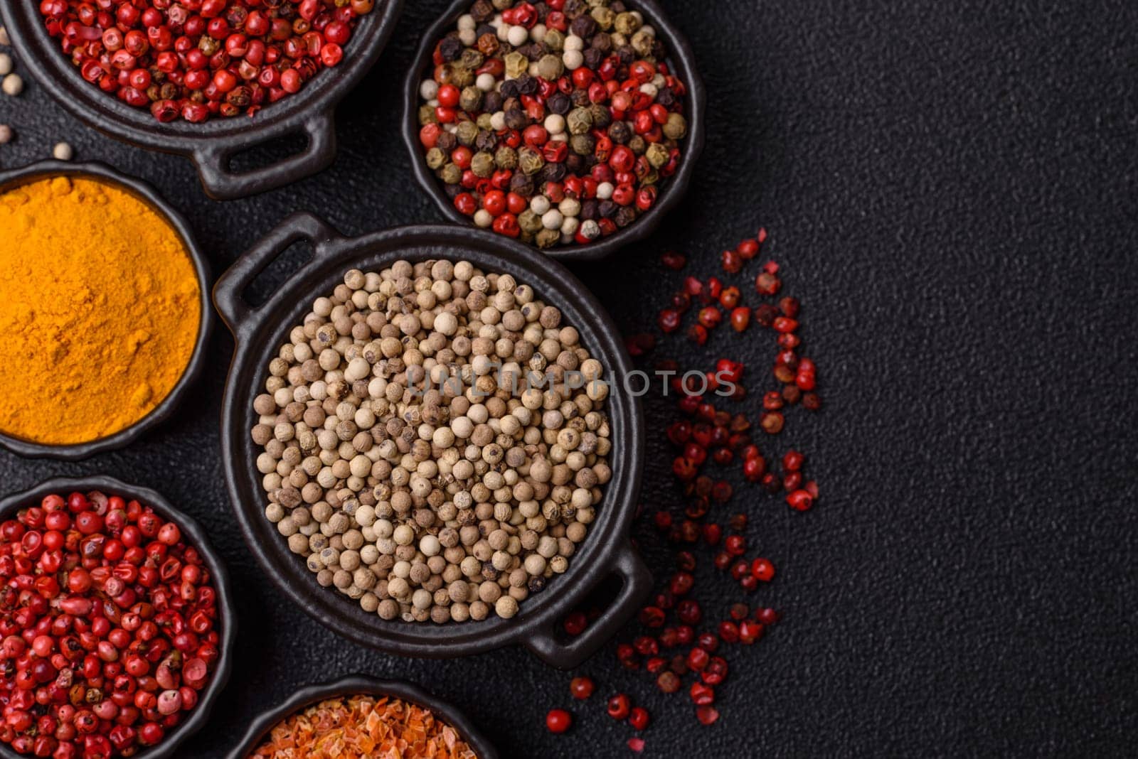 Variations of spices, allspice, turmeric, paprika, salt in ceramic bowls on a dark concrete background