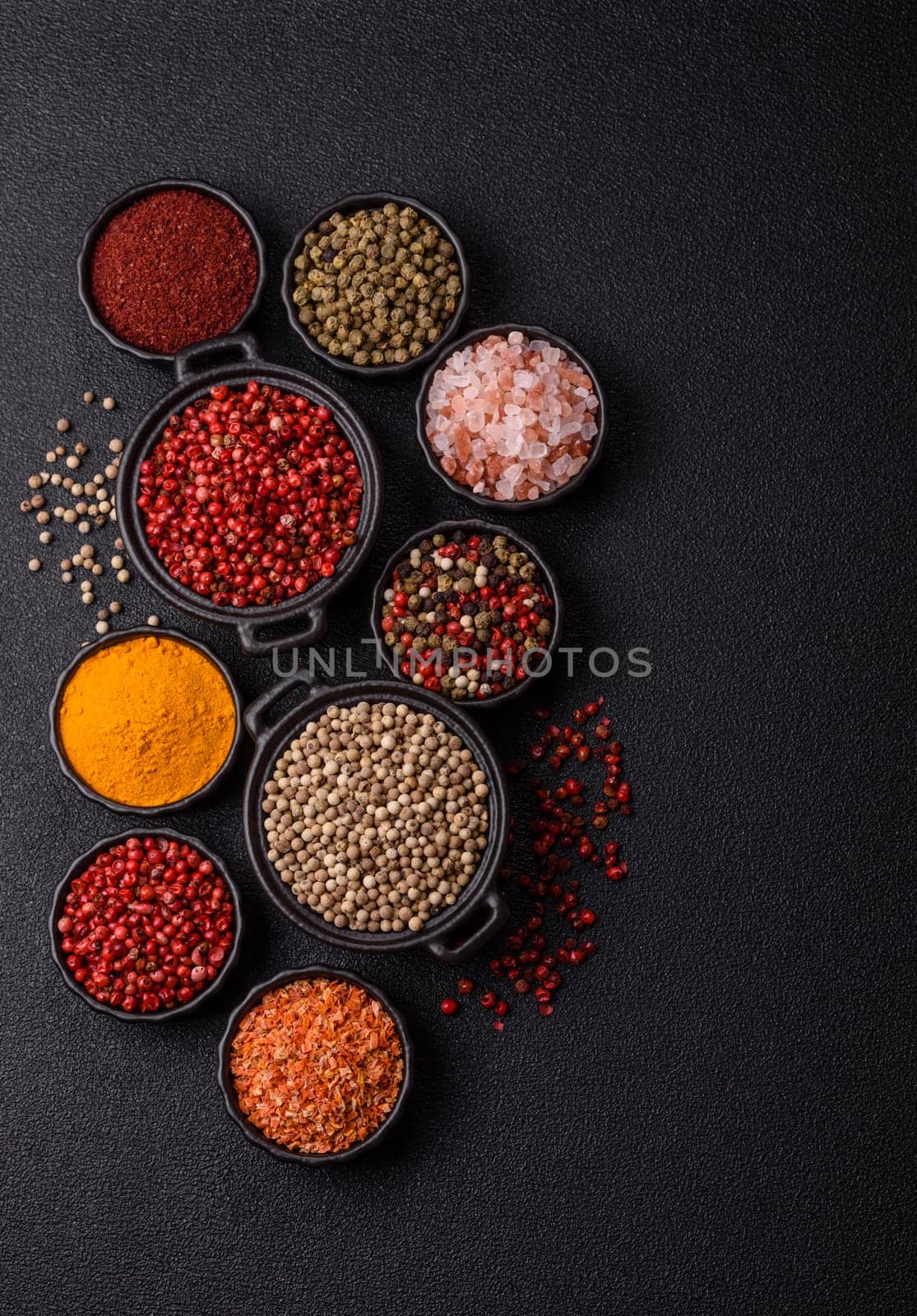 Variations of spices, allspice, turmeric, paprika, salt in ceramic bowls on a dark concrete background