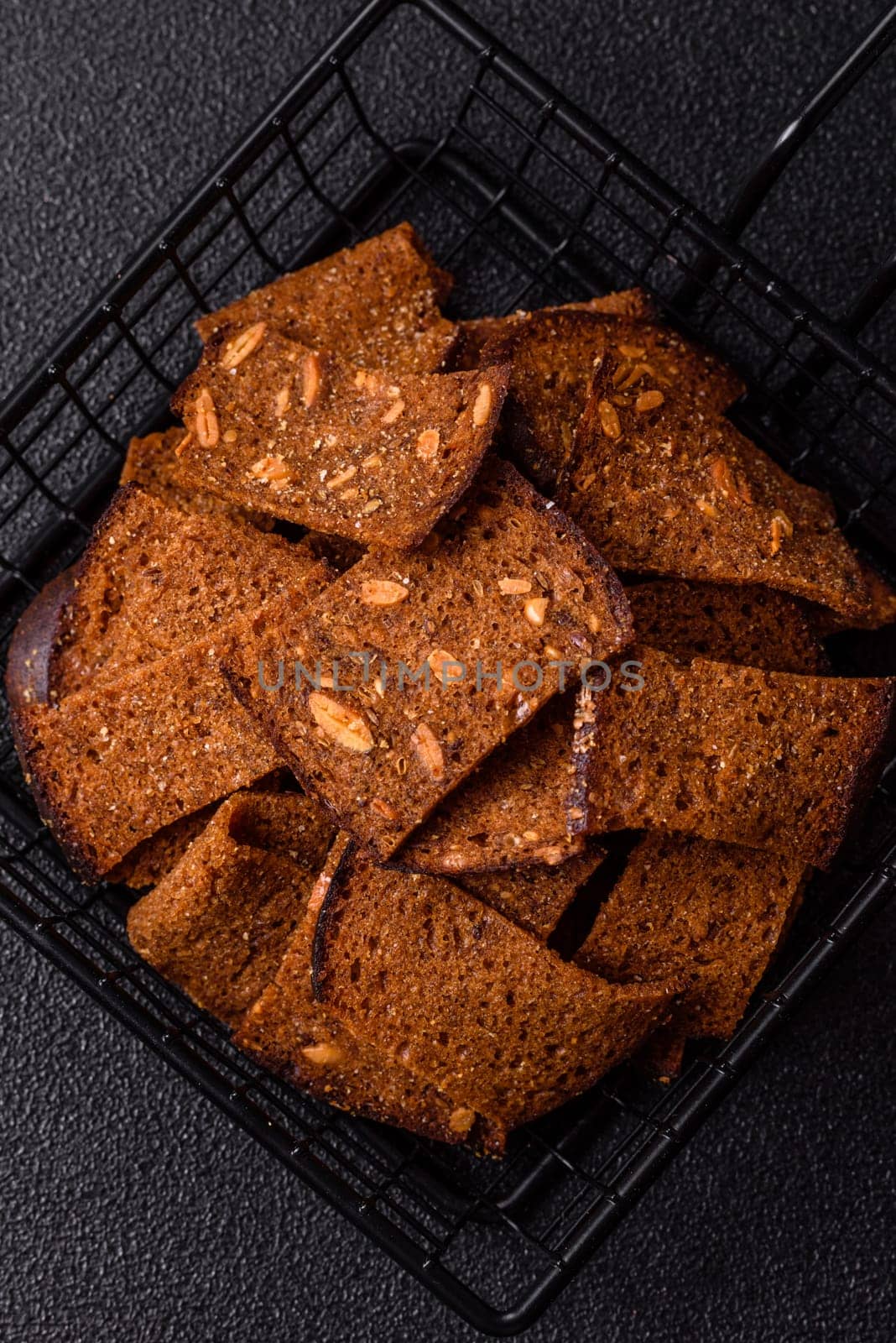 Crispy homemade brown bread chips with seeds and grains, salt, spices and herbs on a dark concrete background