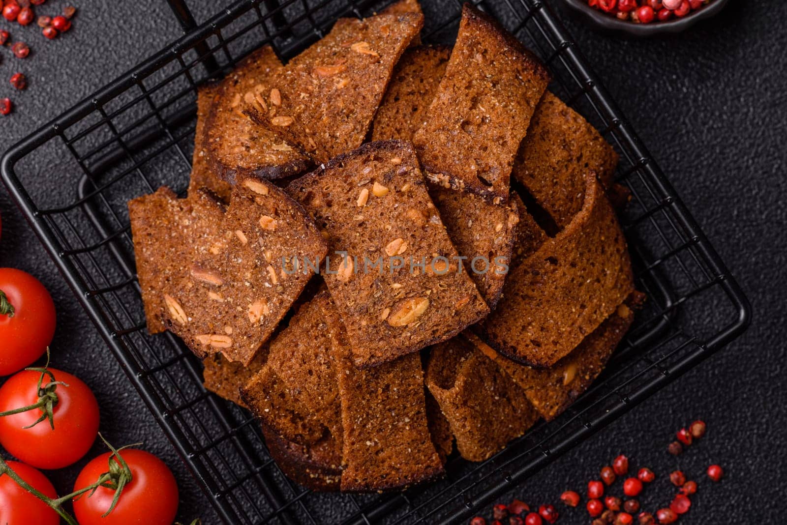 Crispy homemade brown bread chips with seeds and grains, salt, spices and herbs on a dark concrete background