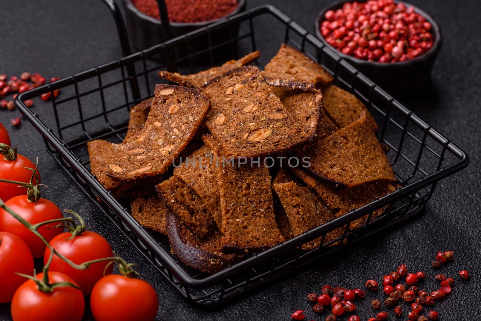 Crispy homemade brown bread chips with seeds and grains, salt, spices and herbs on a dark concrete background