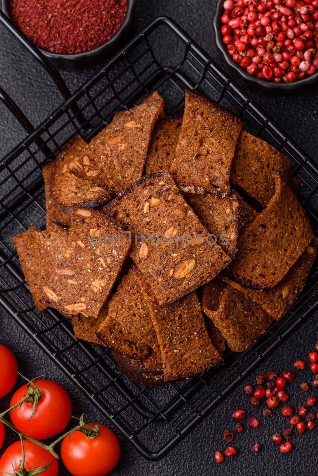 Crispy homemade brown bread chips with seeds and grains, salt, spices and herbs on a dark concrete background