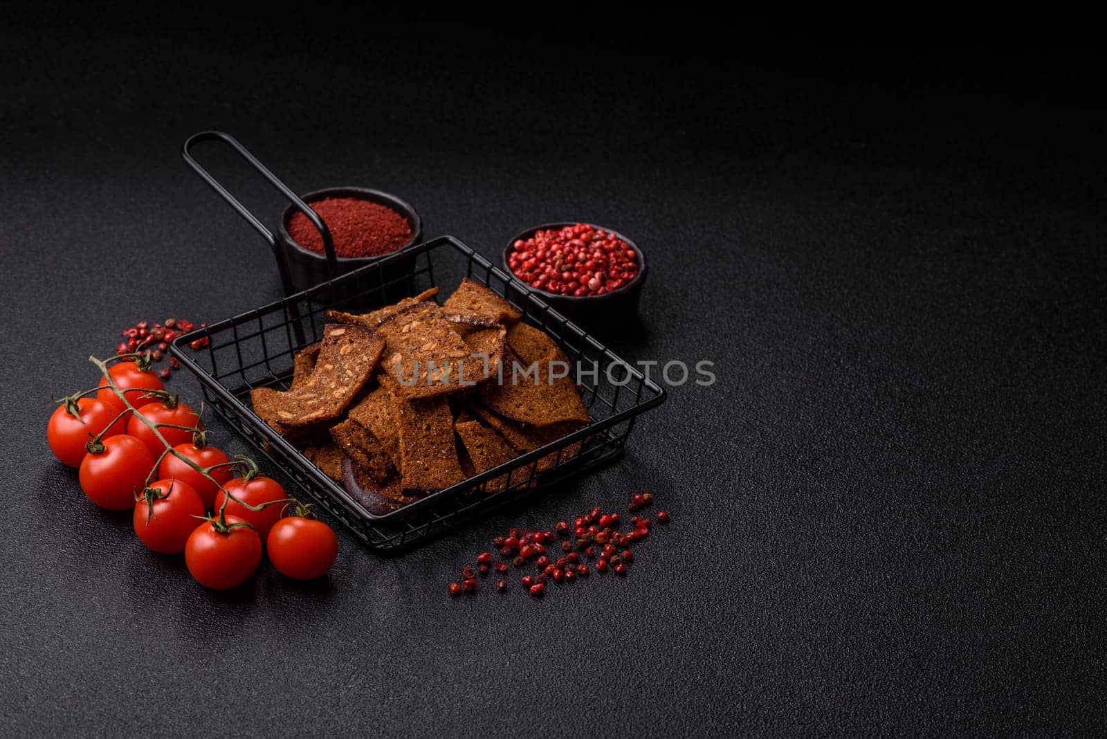 Crispy homemade brown bread chips with seeds and grains, salt, spices and herbs on a dark concrete background