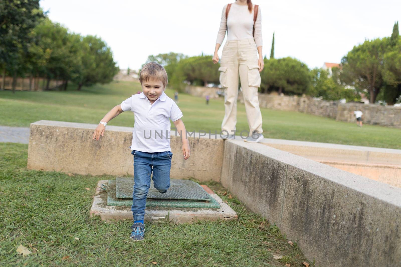 A young boy runs across a grassy field with a woman watching him. The scene is peaceful and joyful, with the boy enjoying his time outdoors
