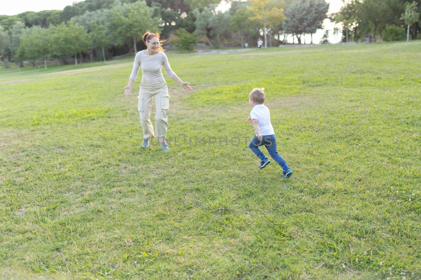 Mother and son are running through a grassy park on a sunny day