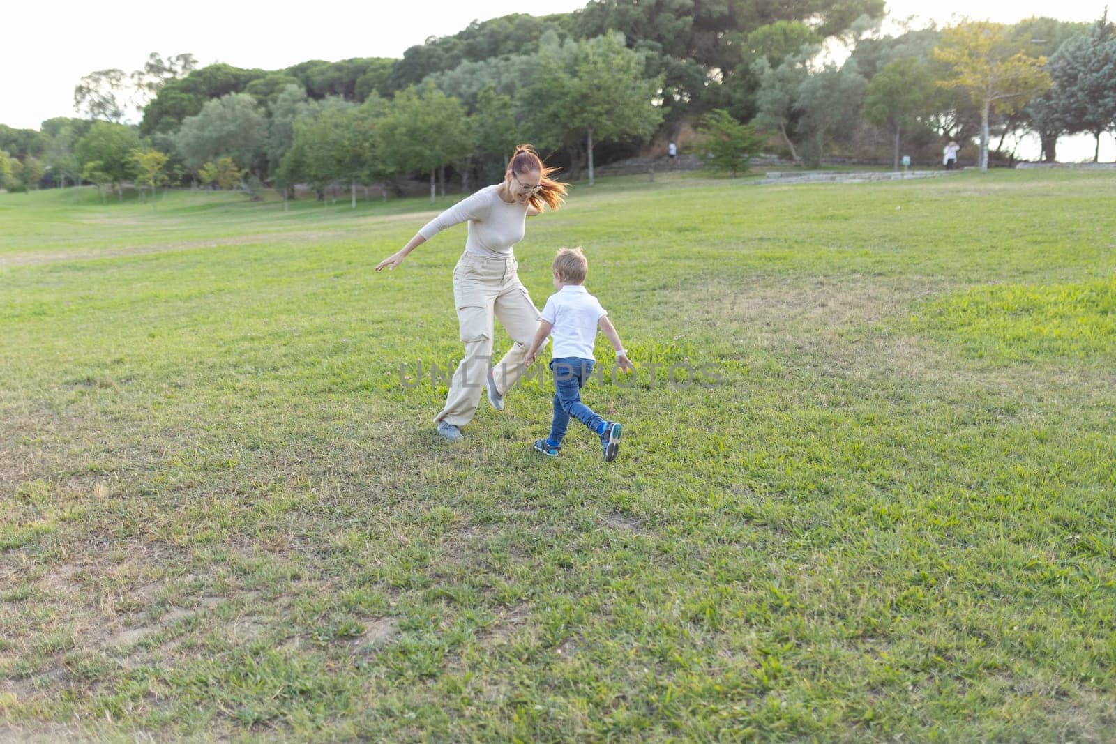 Mother and her son are running through a grassy park, enjoying a beautiful sunny day together