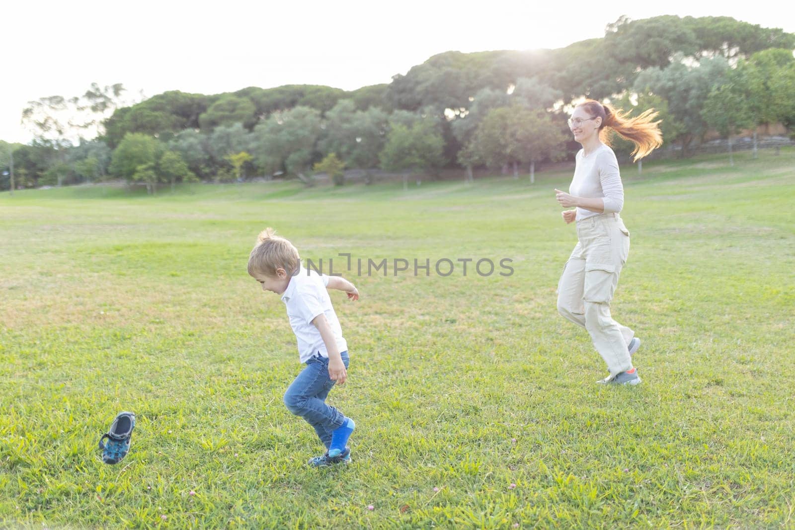 Mother and son having fun playing tag and running on the grass in a park