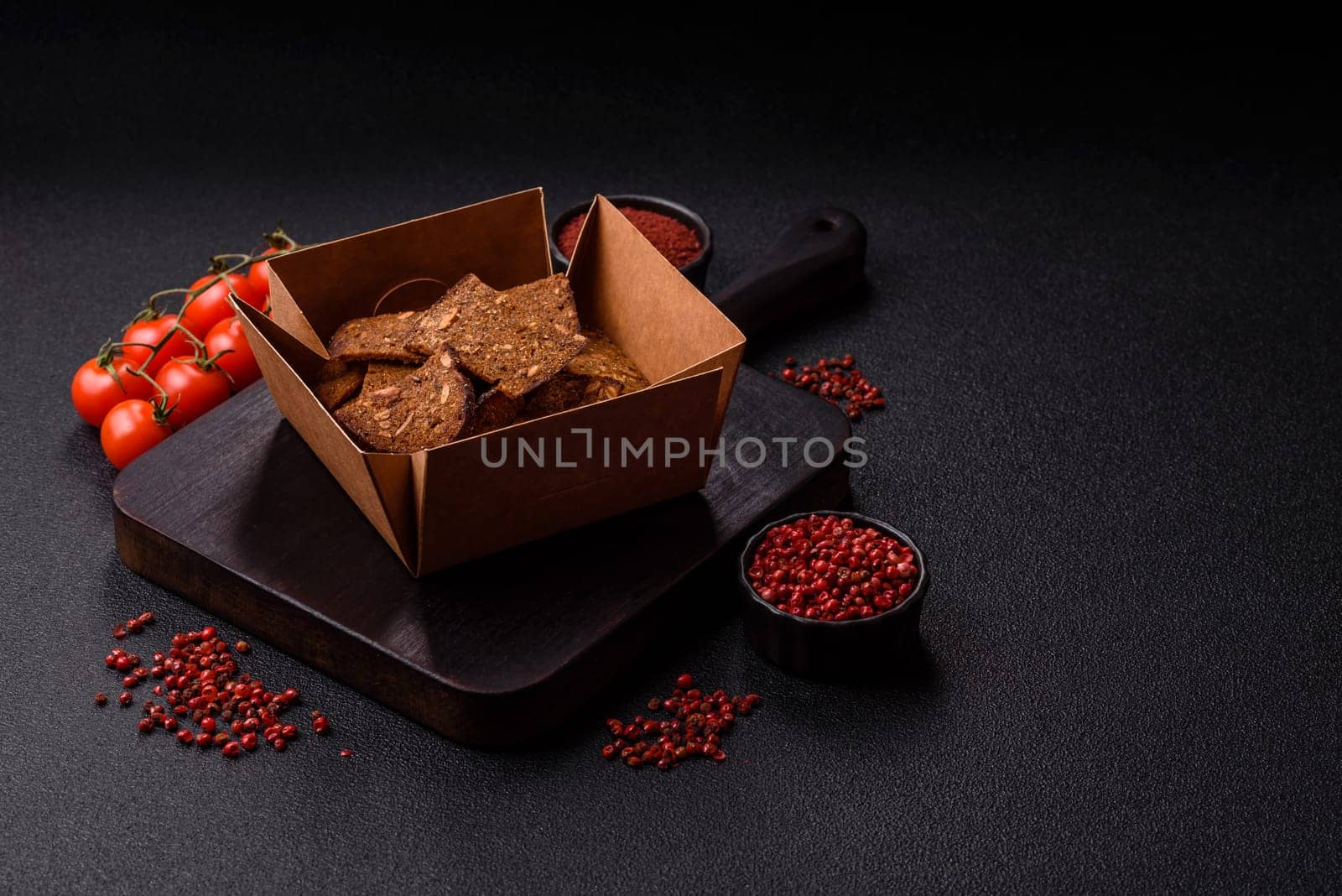 Crispy homemade brown bread chips with seeds and grains, salt, spices and herbs on a dark concrete background