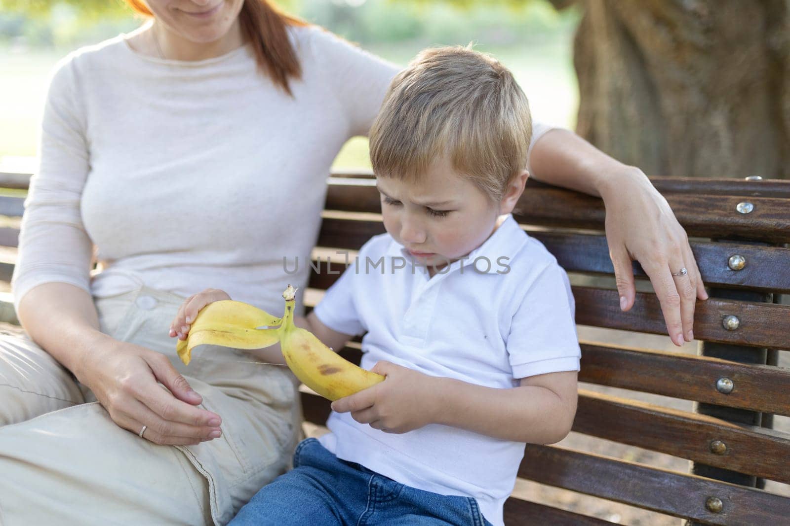 Mother and son spending time together on a bench in a park while discussing and eating a banana