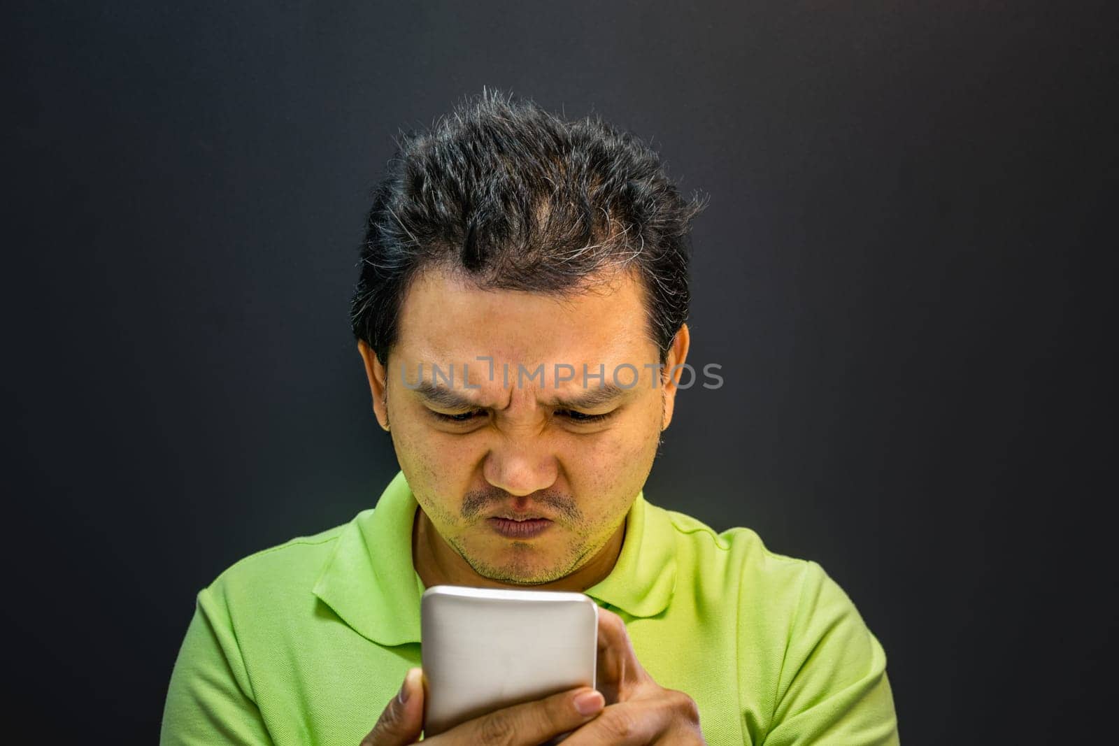 Asian man 40s have a short hair in polo shirt strain have a unhappy gesture with failure and problems concept using smartphone on black background dark style