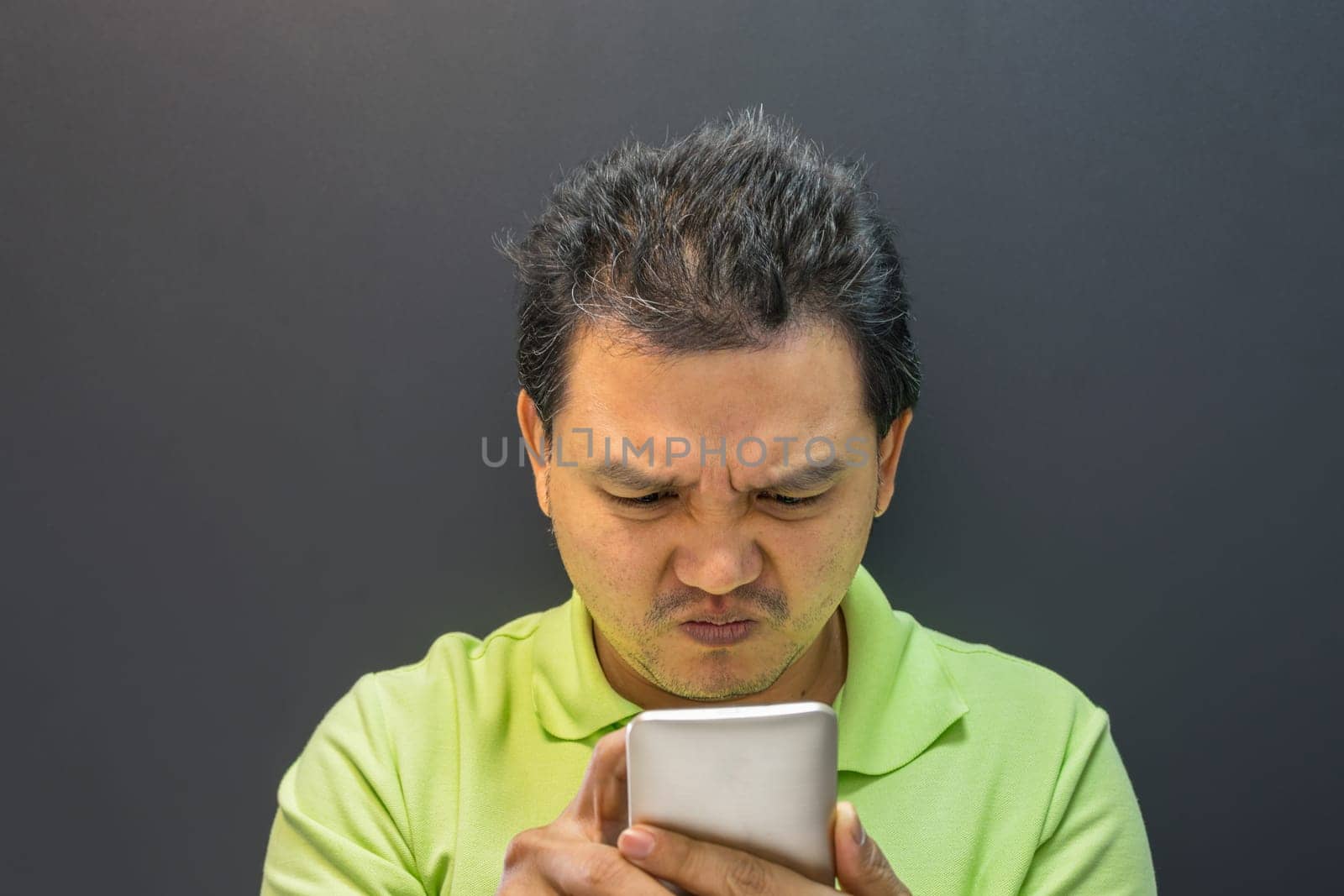 Asian man 40s have a short hair in polo shirt strain have a unhappy gesture with failure and problems concept using smartphone on black background dark style