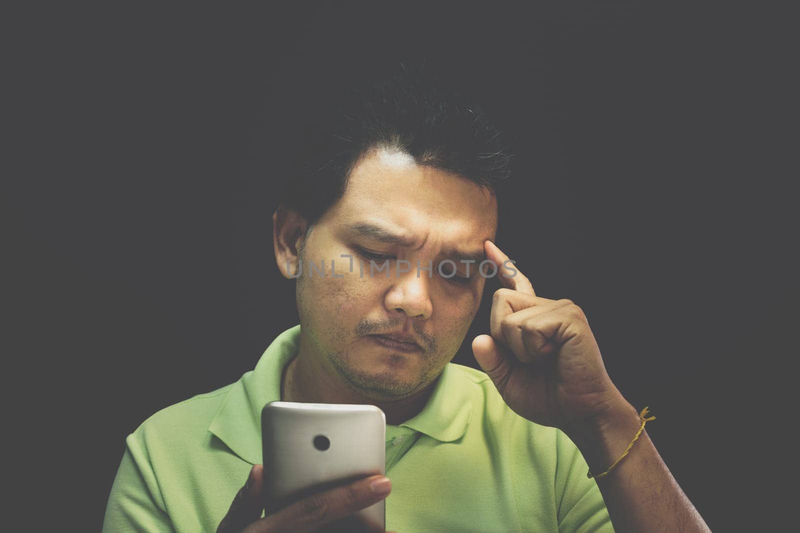 Asian man 40s have a short hair in polo shirt smiling have a thinking gesture with doubt and thoughtful concept using smartphone on black background dark style