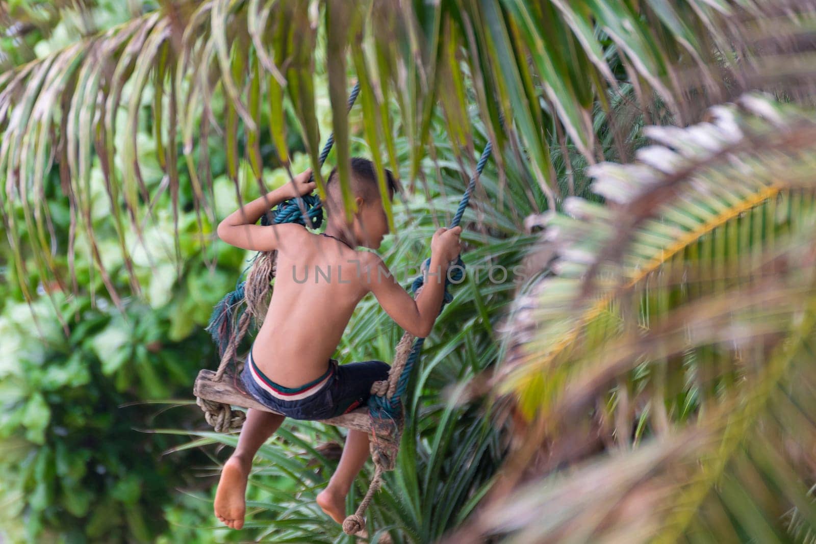 Asian young boy swinging on a rope swing at a beach