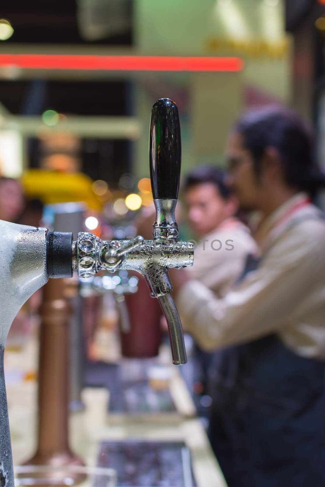 Barman or bartender pouring a draught lager beer from beer tap on counter for serving in a restaurant or pub.