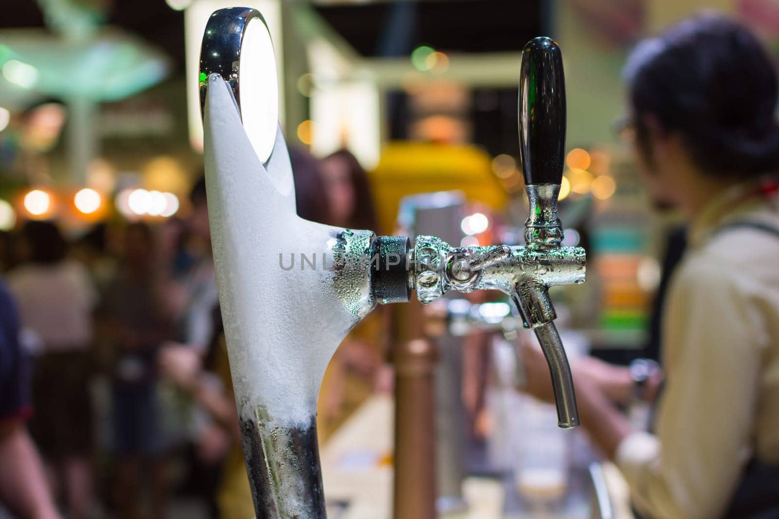 Barman or bartender pouring a draught lager beer from beer tap on counter for serving in a restaurant or pub.