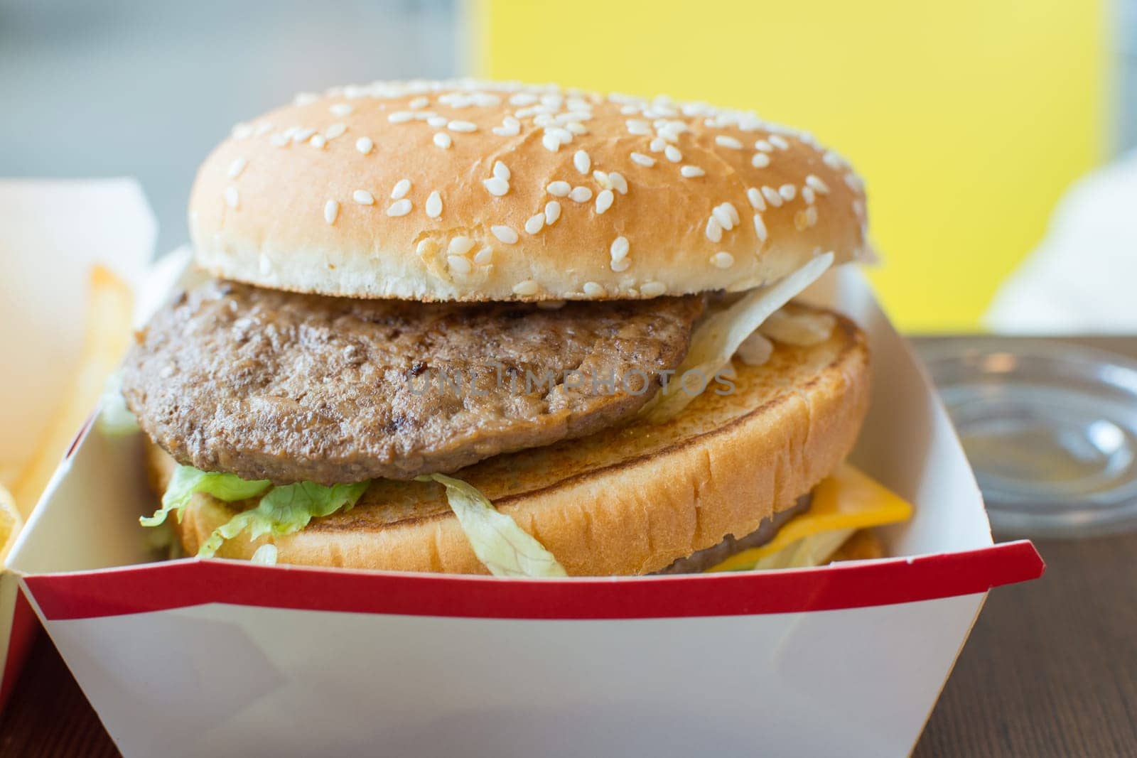 Hamburger is a fast food make from bun, meat, cheese and vegetable in white paper box in restaurant