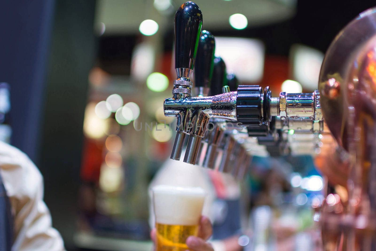 Barman or bartender pouring a draught lager beer from beer tap on counter for serving in a restaurant or pub.