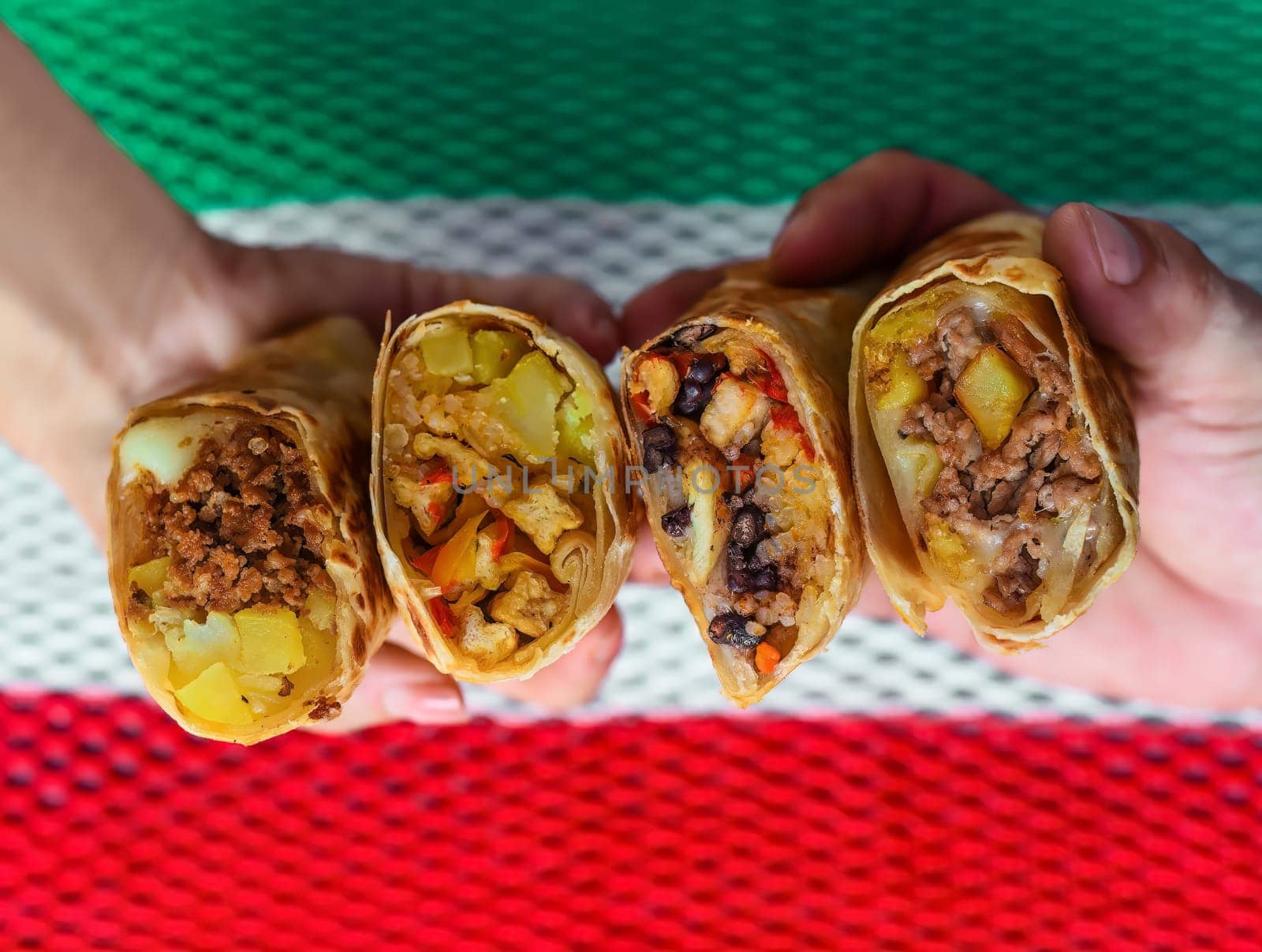 Hands holding Mexican burritos with chorizo, beef, chicken, vegetarian against mexican flag