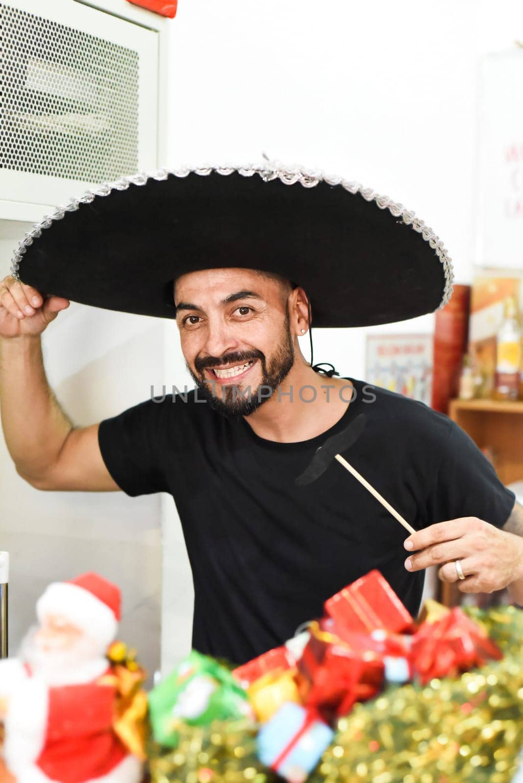 Mexican man in sombrero holding mustache on a stick and smiles in the camera