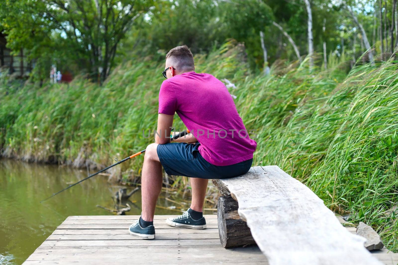 Young fisherman sitting on wooden pier, fishing in the lake. he holding the rod and looking at float